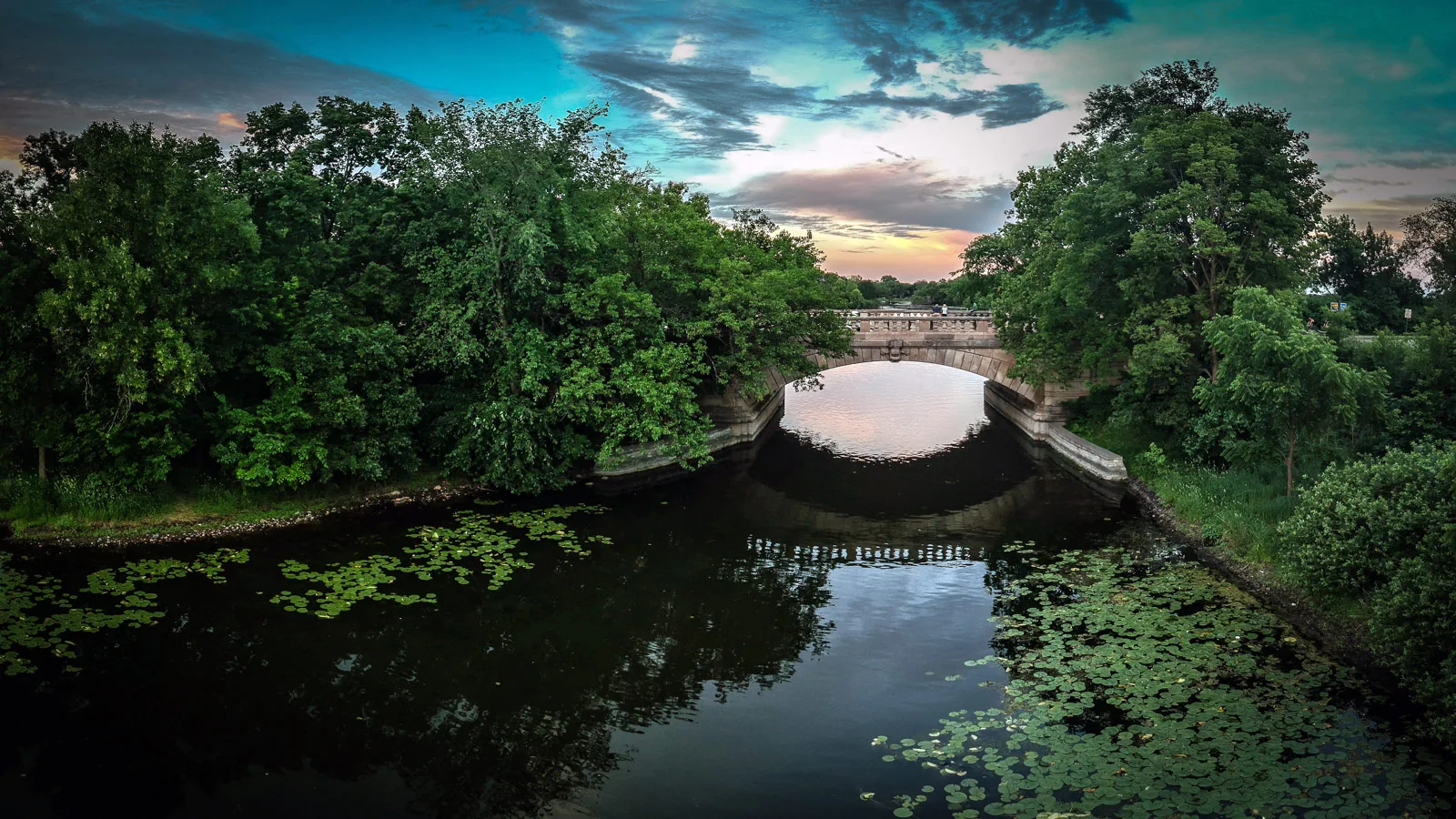 Tree-lined waterway and stone bridge at sunset